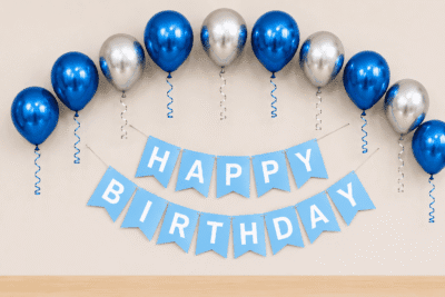 Blue and silver metallic birthday decoration with balloons, ribbon curls and happy birthday banner for party setup.