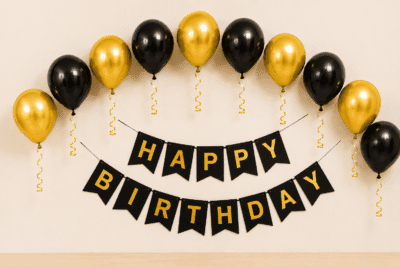 Black and gold happy birthday decoration with metallic balloons, curling ribbons and elegant birthday banner for party setup.