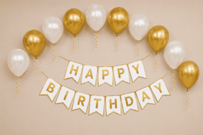 Gold and white happy birthday decoration with metallic balloons, ribbon curls and elegant birthday banner for party setup.