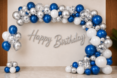 Blue, white and silver birthday balloon decoration with metallic balloon arch, silver confetti balloons, floor balloon cluster and silver cursive Happy Birthday banner.