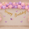 Butterfly theme birthday decoration with pink, purple, peach and white balloons, butterfly stickers and gold Happy Birthday banner.