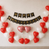 Romantic Happy Anniversary wall decoration with red and white heart-shaped balloons, black and gold banner, and two pink heart foil balloons.
