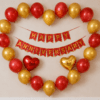 Heart shape Happy Anniversary decoration with red and golden balloons, red and gold cardstock anniversary banner, and red and golden heart foil balloons on a wall backdrop.