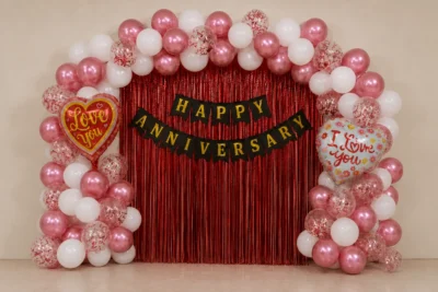 Pink white anniversary decoration setup with balloon arch, red foil curtain, banner and heart balloons