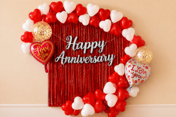 Red and white heart balloon anniversary decoration with red foil curtain, silver Happy Anniversary banner, love you foil balloons and golden confetti balloons.