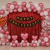 Romantic happy anniversary decoration with red foil curtain backdrop, black and gold cardstock banner, metallic pink and white balloon arch, red confetti balloons, pink heart balloons and love you foil balloons for anniversary celebration.